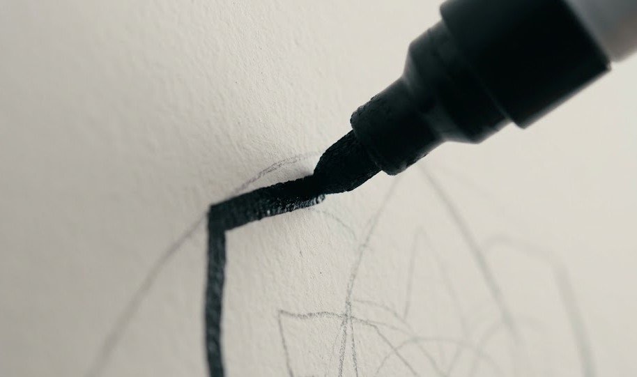 oco detalhado em uma mão segurando uma caneta marcador de tinta à base de água, pronta para iniciar o contorno de como desenhar na parede.