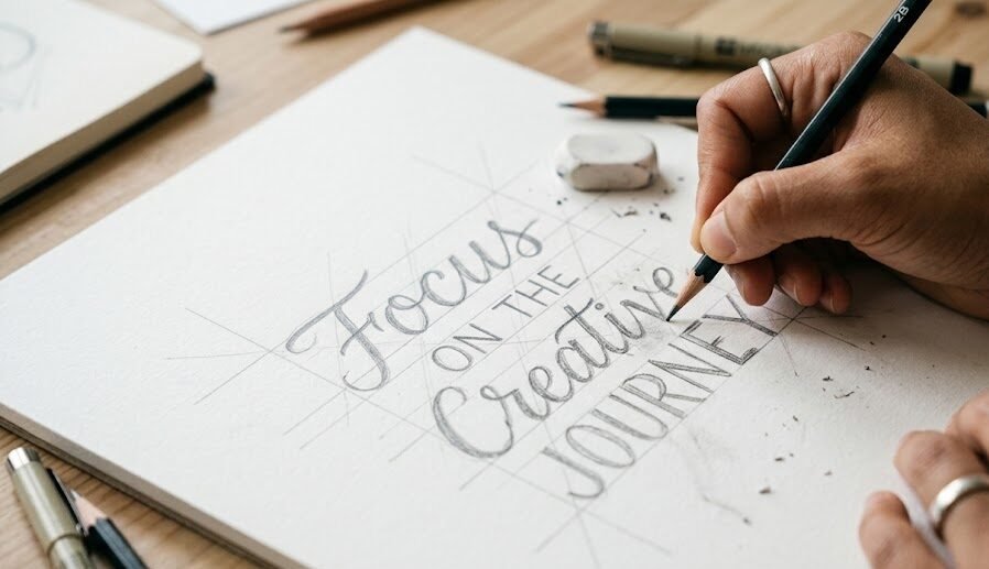Foco nas mãos de um artista criando as linhas de guia e esboços a lápis para estruturar o layout perfeito de uma frase antes de passar a caneta.