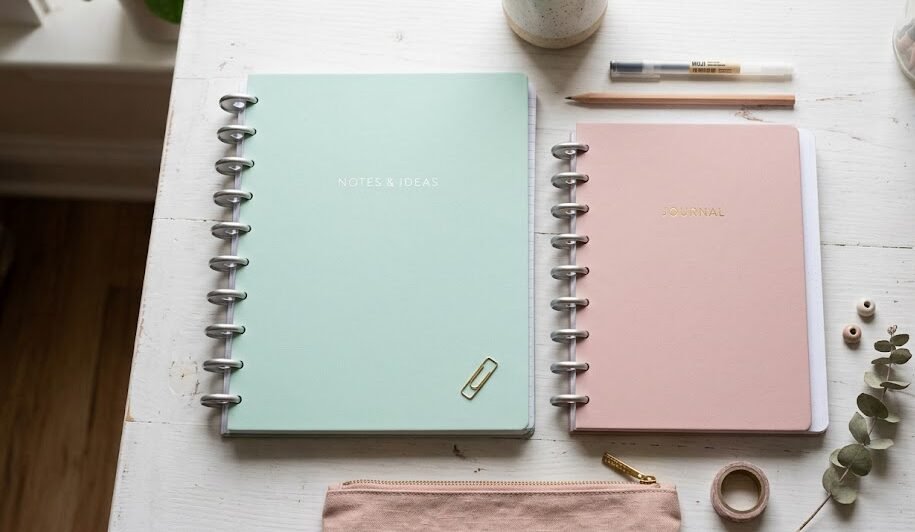 Dois cadernos inteligentes de cores pastel, um tamanho grande universitário e um pequeno A5, lado a lado em uma mesa branca.