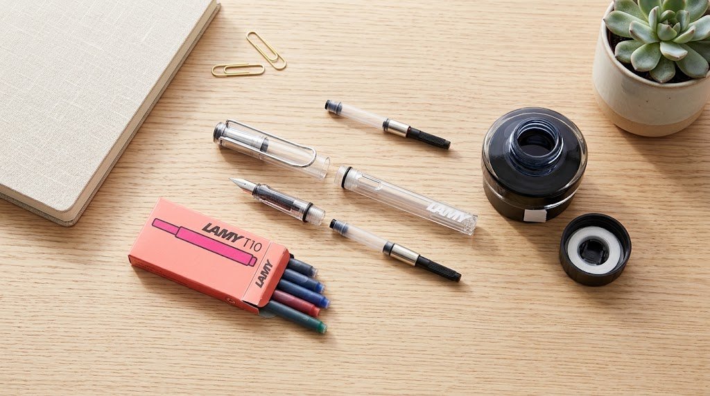 Frasco de tinta Lamy e cartuchos ao lado de uma caneta tinteiro Lamy Safari em cima de uma mesa de madeira.