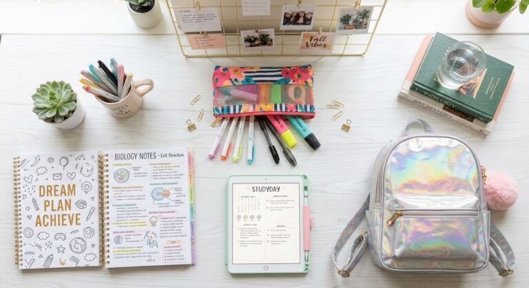 Mochila escolar holográfica com chaveiro de pompom apoiada em uma mesa de estudos com estojo colorido.
